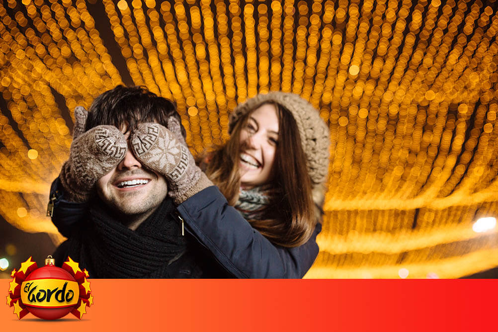 The history of the Spanish Christmas Lottery Young woman covers the eyes of her smiling boyfriend at Christmas time
