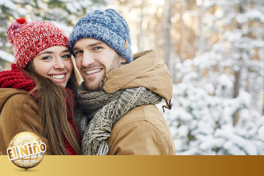 Smiling couple dressed in winter clothes stand outside in the snow