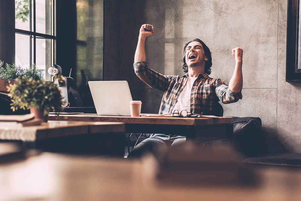 Man seated at desk raises arms in celebration