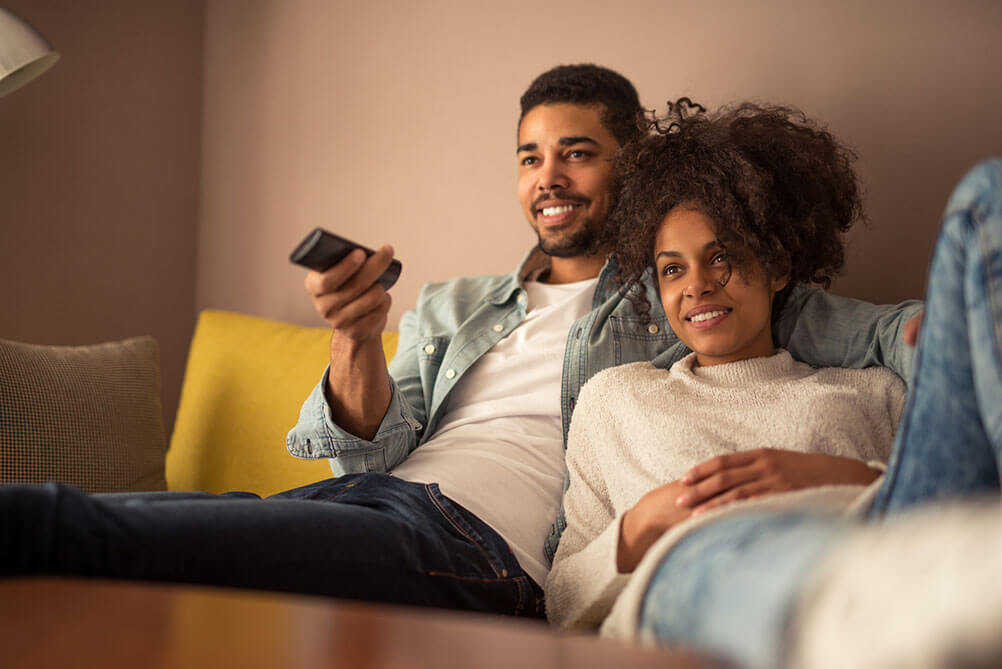 A smiling couple watch TV from their sofa