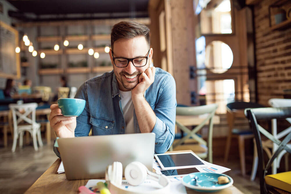Man drinking coffee and smiling at computer screen