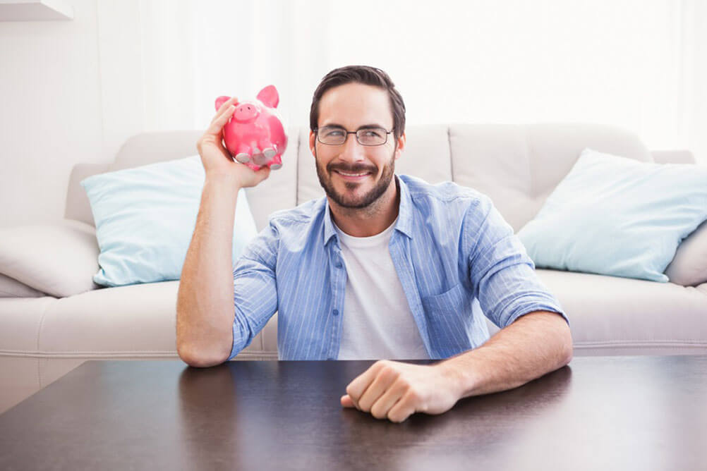 Bearded man smiling and holding piggy bank in one hand. 