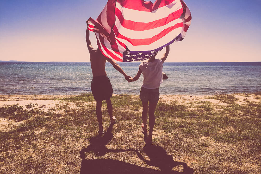 Couple holding American flag and walking towards the sea