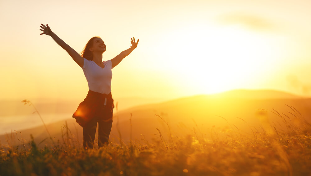 Woman spreads her arms in delight at sunrise