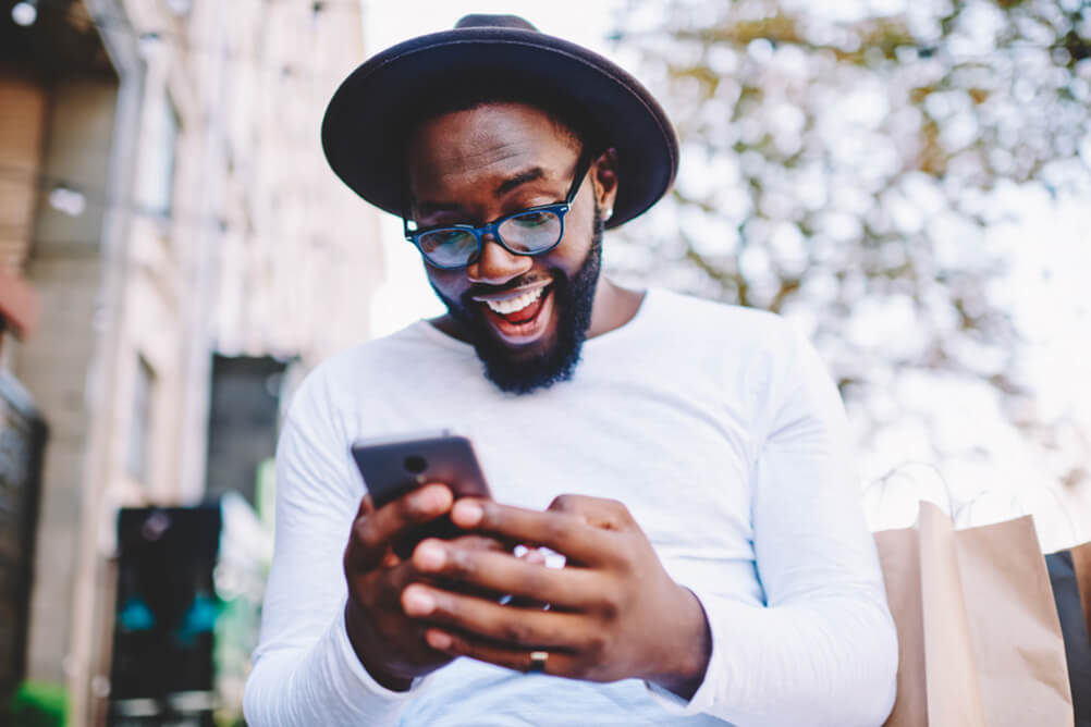 Glasses and hat-wearing man smiles while looking at phone in his hand