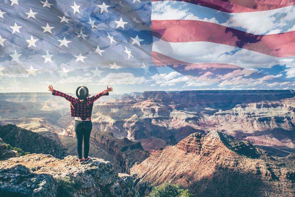 Woman on top of mountain with image of US flag in the sky