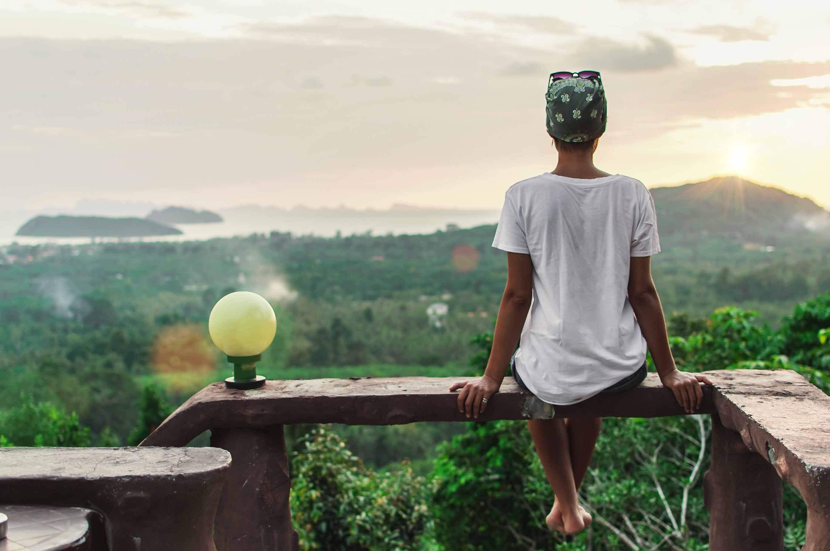 Woman sits on a bench overlooking a jungle at sunset, enjoying a slow travel experience