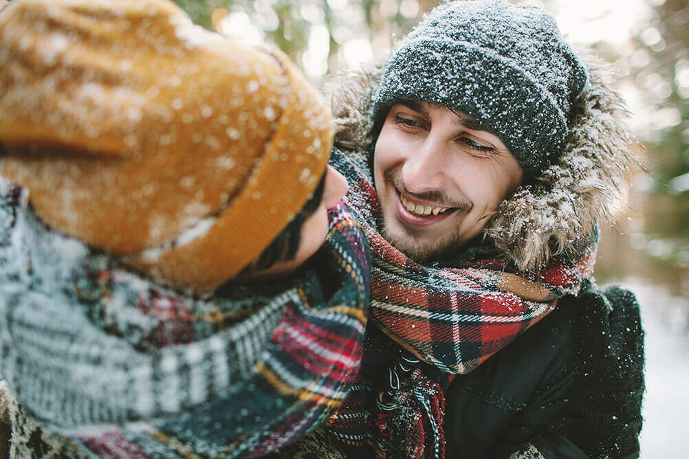 Couple wearing wooly winter clothes embrace in the snow