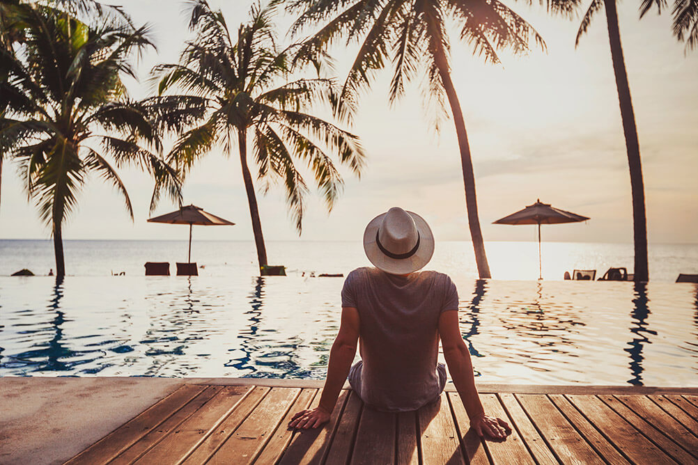 Man in a Panama hat sits on the dock looking out over a tropical seascape