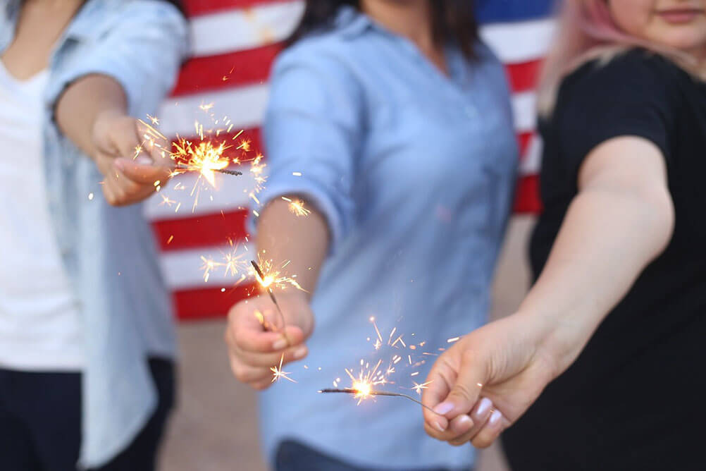 Three people holding sparklers in front of an American flag