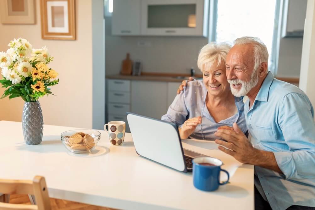 Daily lotteries Smiling couple sitting at the kitchen table and looking at the laptop