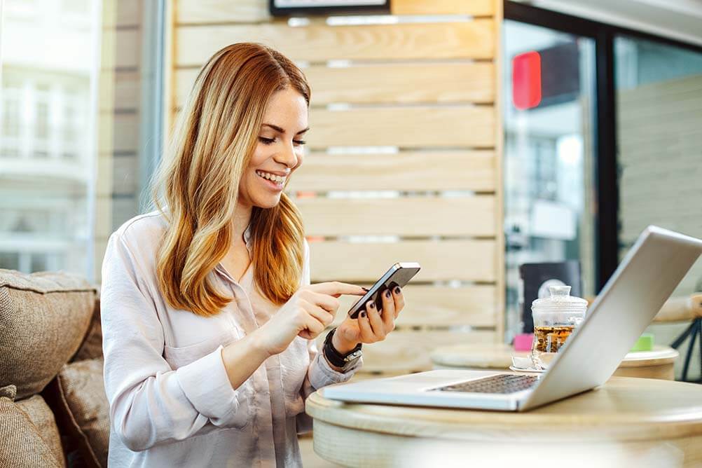 Woman on her phone and laptop checking Lottoland Payment Methods