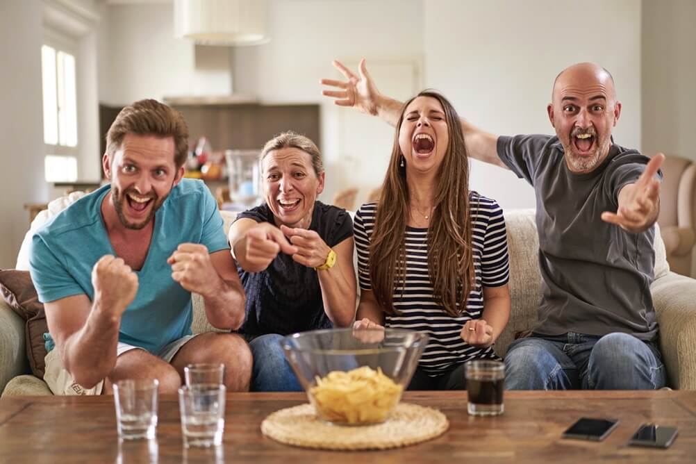 Family of four watching football and cheering around the TV 