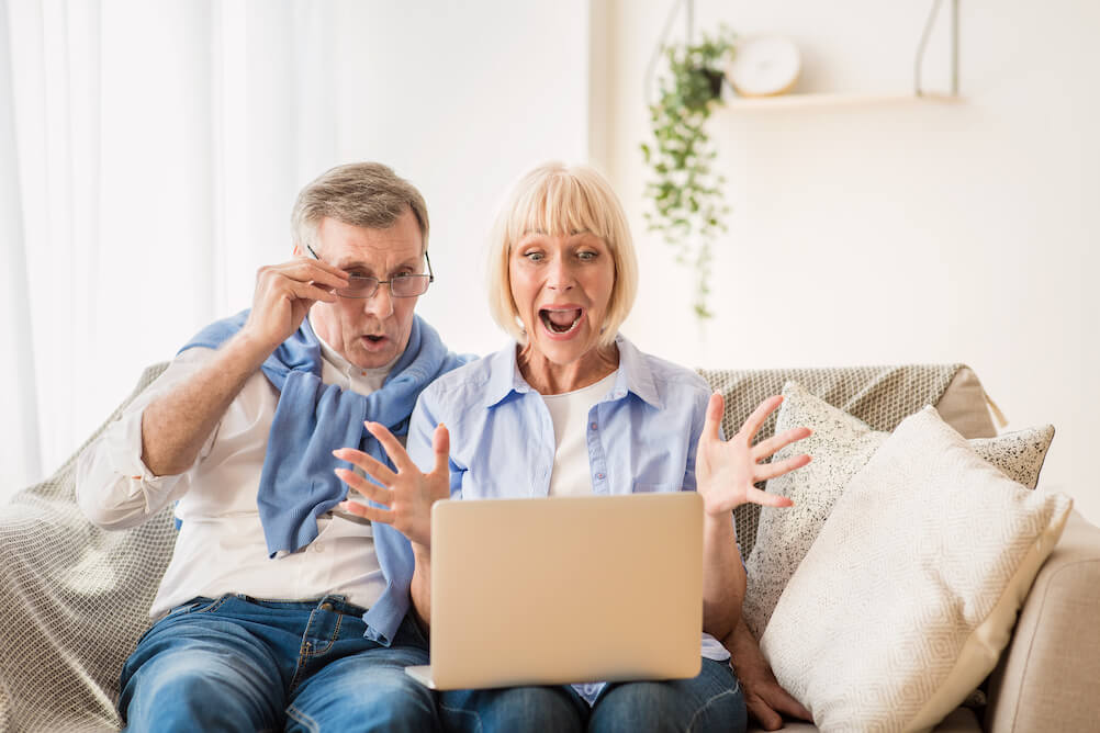 Surprised elder couple checking lottery ticket prices on their laptop