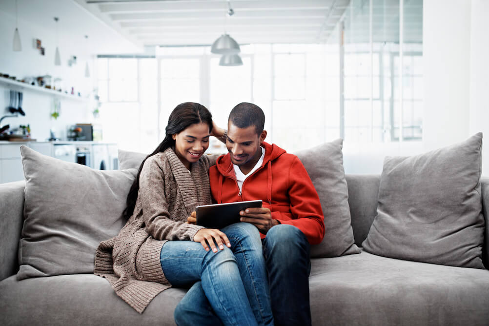 Couple sat on sofa sharing a tablet claiming winnings 