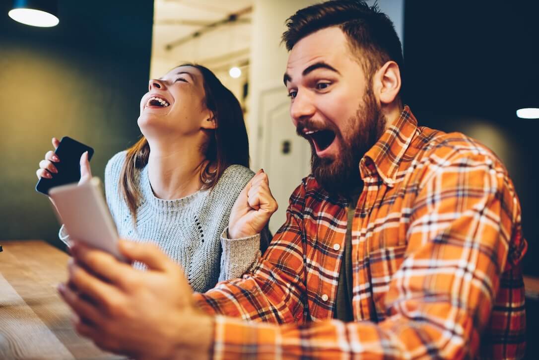 Excited Megaways players Ein aufgeregter Mann und eine aufgeregte Frau spielen einen Megaways-Slot auf ihrem Handy.